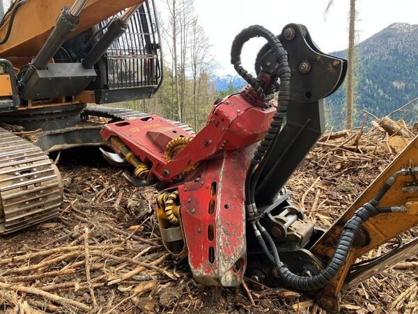 A large forestry machine with a red and black color scheme operating in a wooded mountainous area.