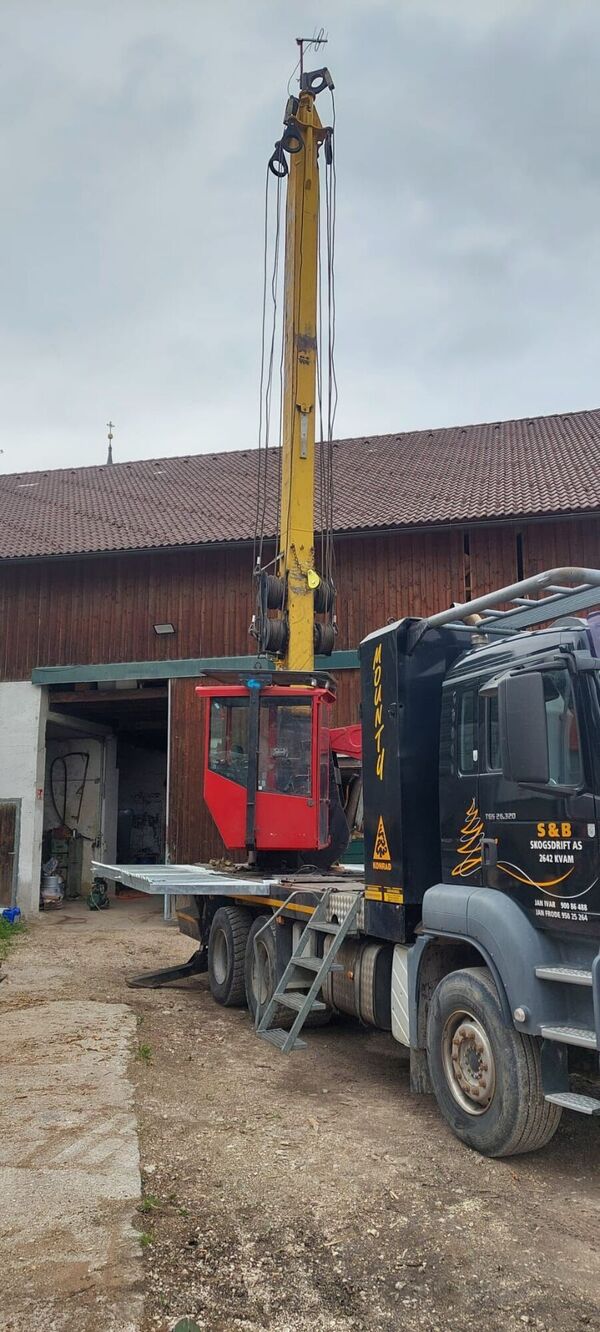 A red and yellow crane mounted on a truck in front of a barn