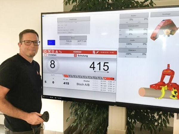 Man standing beside a large digital display showing industrial data and a machinery component