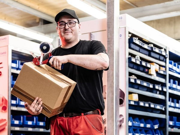 A man wearing glasses and a cap holding a parcel in a warehouse