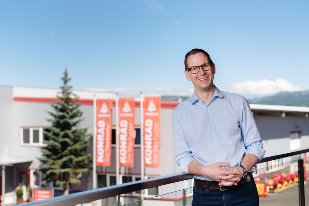Markus Konrad standing casually in front of an industrial building with company banners