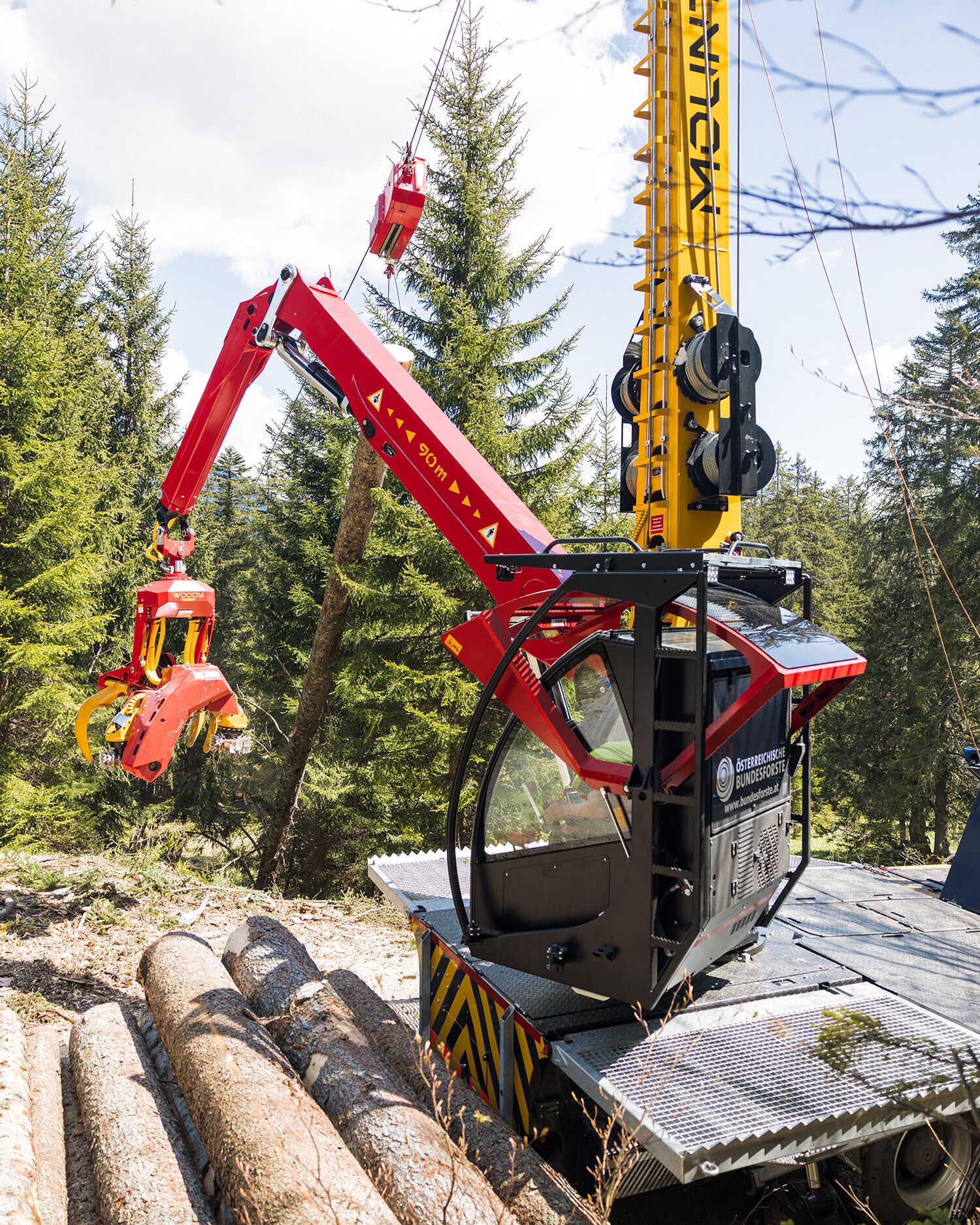 Ein Forstkran mit einer Kralle hebt Holzstämme in einem dichten Waldgebiet