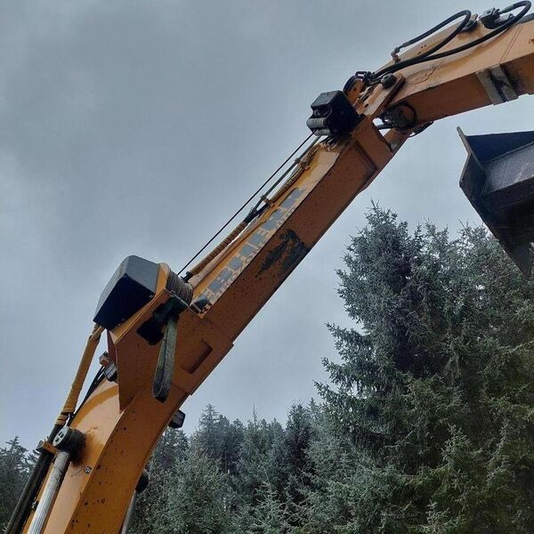 A close-up view of an excavator arm against a forest backdrop