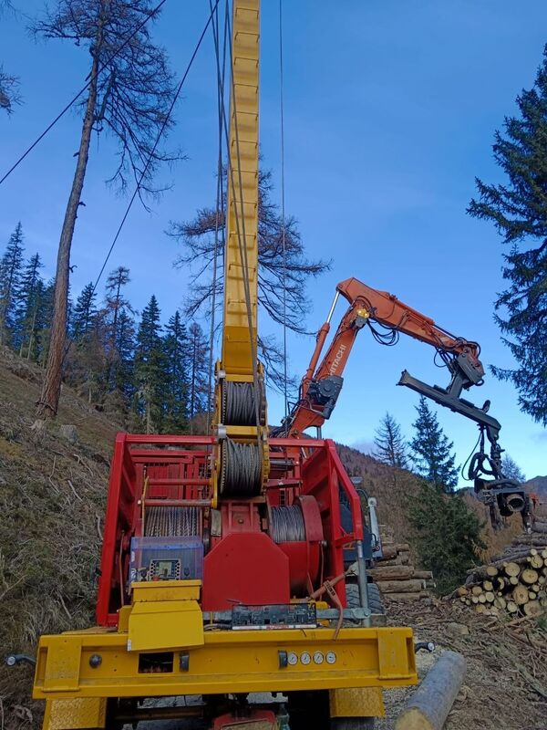 A large yellow piece of forestry equipment with a crane arm operating in a forest