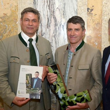Two men in traditional attire holding an award and a booklet related to forest strategy