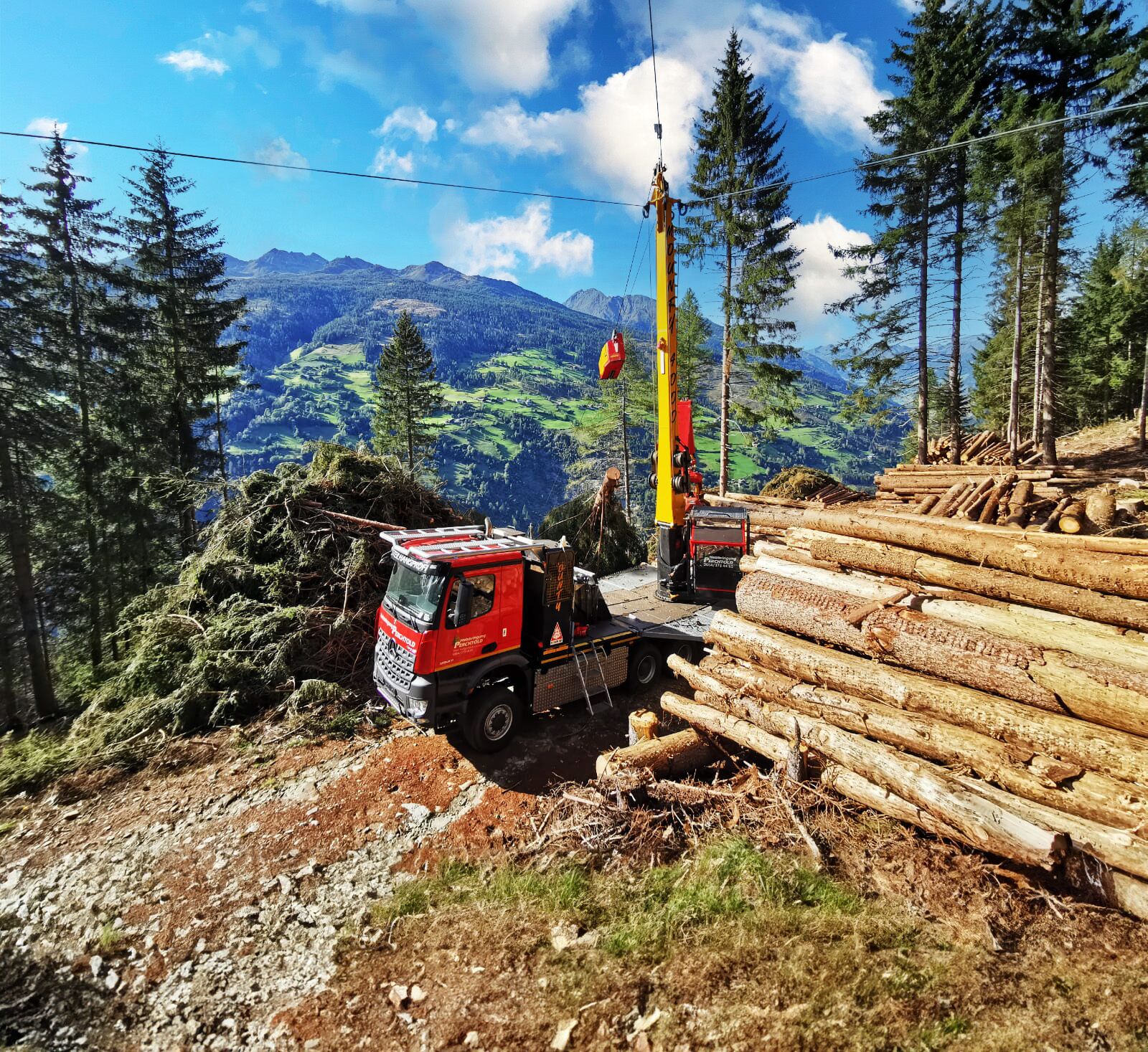 An image depicting a mountainous forest landscape where trucks are being loaded with cut timber logs.