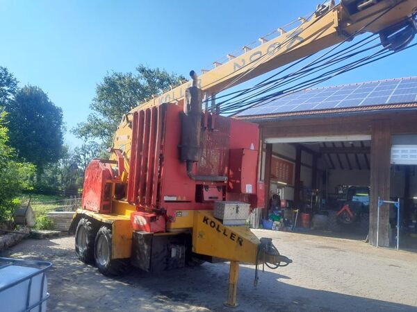 A red heavy-duty forestry machine beneath a crane near a workshop