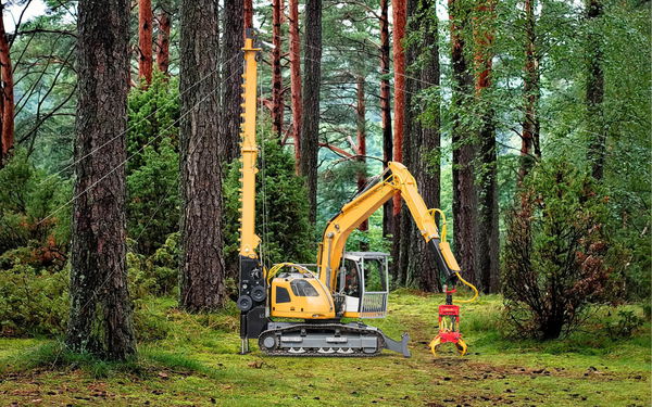 Yellow excavator and pile driver amidst lush green forest with tall trees