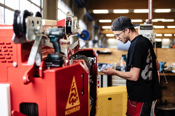 Ein Techniker arbeitet an einer roten Maschine in einer Werkstatt mit sichtbarem Konrad-Forsttechnik-Logo.